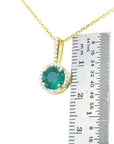 Gold pendant with a round cut colombian emerald next to a ruler on a white background.