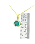Gold pendant with a round cut colombian emerald next to a ruler on a white background.
