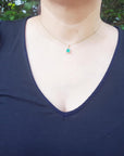 A woman wearing an emerald pendant necklace in a navy blue dress against a green leafy background.