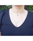 A woman wearing an emerald pendant necklace in a navy blue dress against a green leafy background.