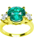 A three stone round cut emerald ring with round side diamonds in 18k yellow gold, on a front position, top view,