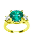 A GIA certified F1 round cut colombian emerald ring three stone with round side diamonds in 18k yellow gold.
