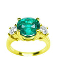 A GIA certified F1 round cut colombian emerald ring three stone with round side diamonds in 18k yellow gold.