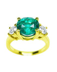 A GIA certified F1 round cut colombian emerald ring three stone with round side diamonds in 18k yellow gold.