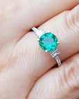A round cut natural Colombian emerald ring on a finger.