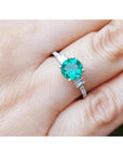 A round cut natural Colombian emerald ring on a finger.