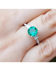 1.10 ct. round Colombian emerald ring with baguette side diamonds in 14K white gold on a hand.