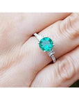 1.10 ct. round Colombian emerald ring with baguette side diamonds in 14K white gold on a hand.