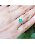 Round cut Colombian emerald ring with baguette side diamonds in 14K white gold on a hand.