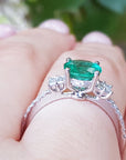Emerald ring with diamond accents on a hand against a blurred green background.