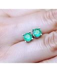 0.89 ct. round Colombian emerald stud earrings in 14k white gold, held on a hand.