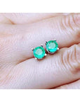 0.89 ct. round Colombian emerald stud earrings in 14k white gold, held on a hand.