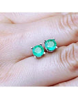 0.89 ct. round Colombian emerald stud earrings in 14k white gold, held on a hand.