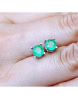 0.89 ct. round Colombian emerald stud earrings in 14k white gold, held on a hand.