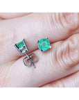 Round 0.89 ct. green emerald stud earrings in 14k white gold, displayed on a hand.