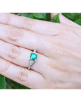 Hand wearing a women's three stone emerald ring against a green leafy background.