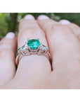 1.00 ct. round emerald ring with trillion side diamonds on a hand, 14K white gold.