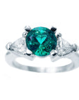 This round cut emerald ring with trillion side diamonds white gold has a top profile sides view.