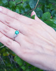 Hand wearing a three stone emerald ring for women with a green leafy background.
