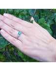 1.00 ct. round emerald ring with trillion side diamonds on a hand, 14K white gold.