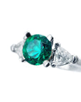 A natural emerald ring round cut with trillion side diamonds displaying its left side profile.