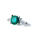 A natural emerald ring round cut with trillion side diamonds displaying its left side profile.
