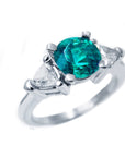 This natural emerald ring round cut with trillion side diamonds displays its top and right-side profile.