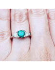 A lady's three stone natural colombian emerald ring round cut on a person's finger.