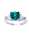 This round cut colombian emerald ring with trillion side diamonds is made of 14k white gold.