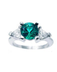 This round cut colombian emerald ring with trillion side diamonds is made of 14k white gold.