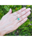 Round-cut natural emerald pendant necklace with halo diamonds in 14K yellow gold, worn on a hand.