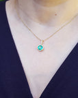 Gold necklace with a round cut emerald pendant on a woman's neck wearing a dark blue top.