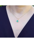 Round-cut natural emerald pendant necklace with halo diamonds on a 14K yellow gold chain.