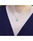 Round-cut natural emerald pendant necklace with halo diamonds on a 14K yellow gold chain.