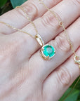 Gold necklace with a colombian emerald pendant on a hand against a green leafy background.