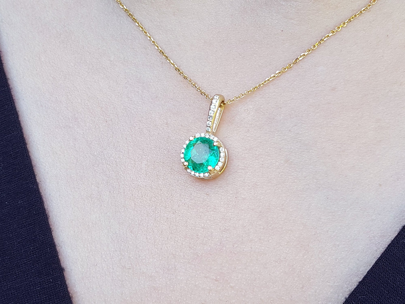 Gold necklace with a natural round emerald pendant on a person's neck.
