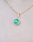 Gold necklace with a natural round emerald pendant on a person's neck.