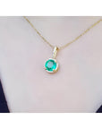 Round-cut natural emerald pendant necklace with halo diamonds on a 14K yellow gold chain.