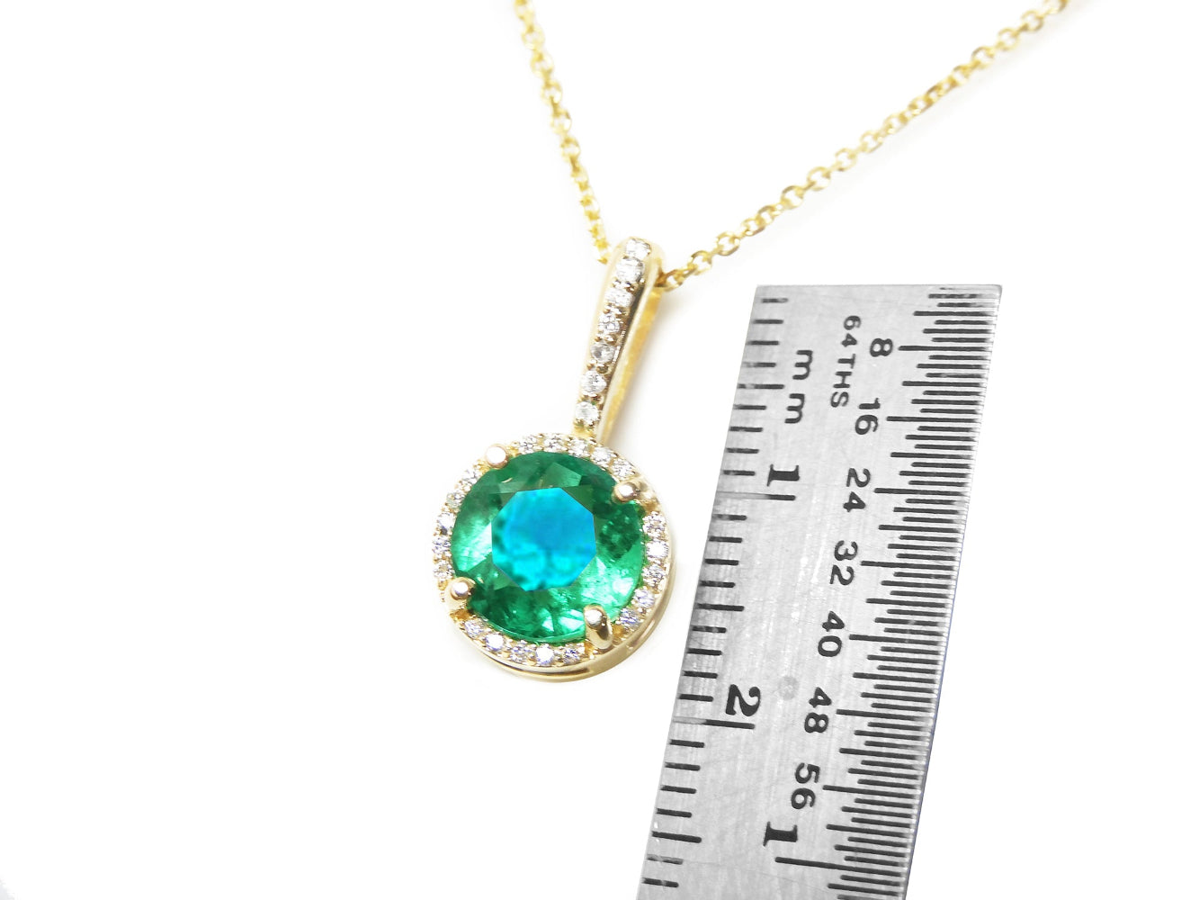 Gold necklace with a round cut emerald pendant next to a ruler for scale on a white background.