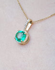Gold necklace with a round cut natural colombian emerald pendant on a light pink skin background,