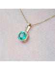 Gold necklace with a round cut natural colombian emerald pendant on a light pink skin background,