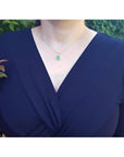 Woman wearing a 14K yellow gold pendant necklace with a round-cut green emerald and halo diamonds.