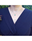 Woman wearing a 14K yellow gold pendant necklace with a round-cut green emerald and halo diamonds.