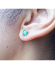 An earlobe wearing a round cut natural Colombian emerald stud earring in 14k gold.