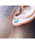 An earlobe wearing a round cut natural Colombian emerald stud earring in 14k gold.