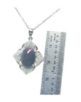Jewelry pendant with a black opal and silver accents, next to a ruler for scale on a white background