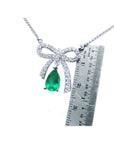 Necklace with a bow and emerald pendant next to a ruler for scale on a white background