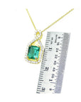 Gold necklace with a natural emerald gemstone pendant next to a ruler for scale on a white background