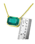Emerald-cut Colombian emerald solitaire necklace in 18K yellow gold, shown with a ruler for scale.