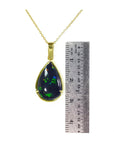 Teardrop-shaped black opal pendant on a gold chain with a ruler for scale.